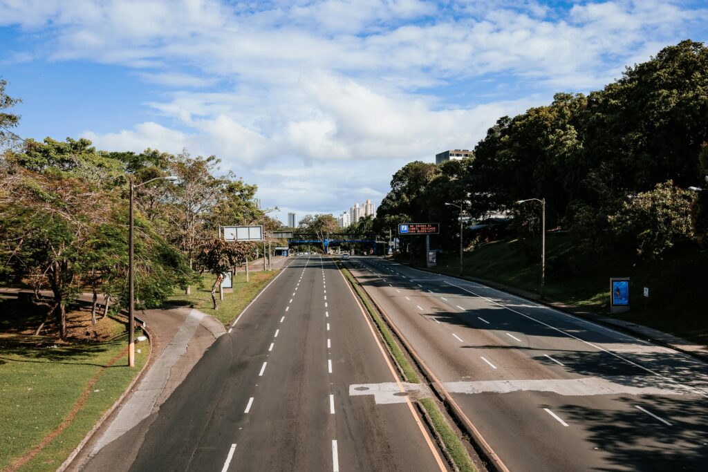 An empty highway lined with greenery, captured in clear daylight under blue skies.